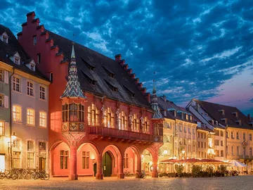 Rathaus beleuchtet, umgeben von Gebäuden und Abenddämmerung.