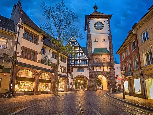 Alte Stadtgebäude umgeben einen Uhren-Turm in der Dämmerung.