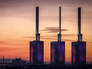 Drei Schornsteine stehen vor einem bunten Sonnenuntergang.