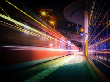 Zug fährt durch eine beleuchtete Station in der Nacht.