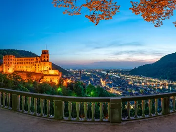 An illuminated castle stands above a city on the river.