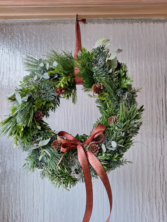 Weihnachtskranz mit rotem Band an Tür.