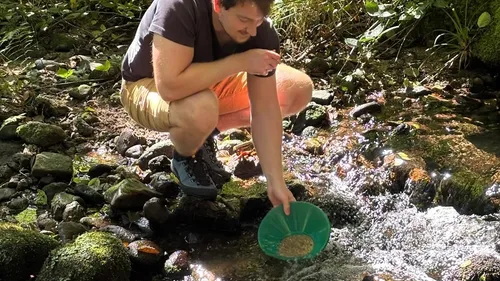 Person schürft in einem Bach nach Gold.