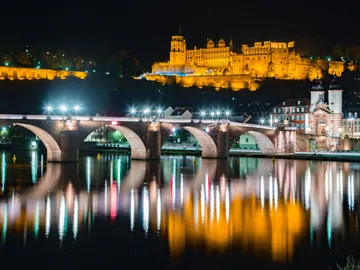 Bridge reflects lights under an illuminated castle.
