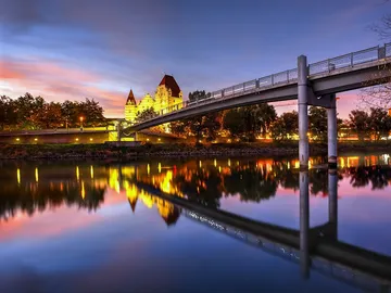 Brücke über ruhiges Wasser mit reflektierendem Gebäude im Hintergrund.