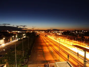 Bahngleise leuchten in der Dämmerung, umgeben von Städten.