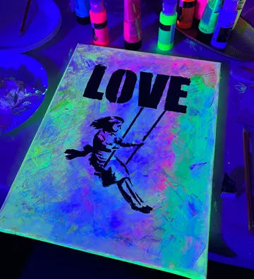 Canvas painting under UV light with text 'LOVE'.