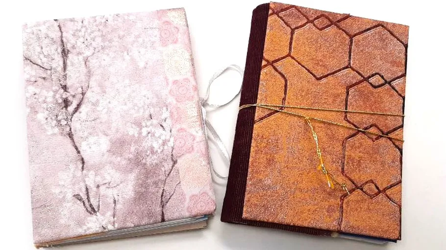 Zwei Hefte mit dekorativen Einbänden nebeneinander.