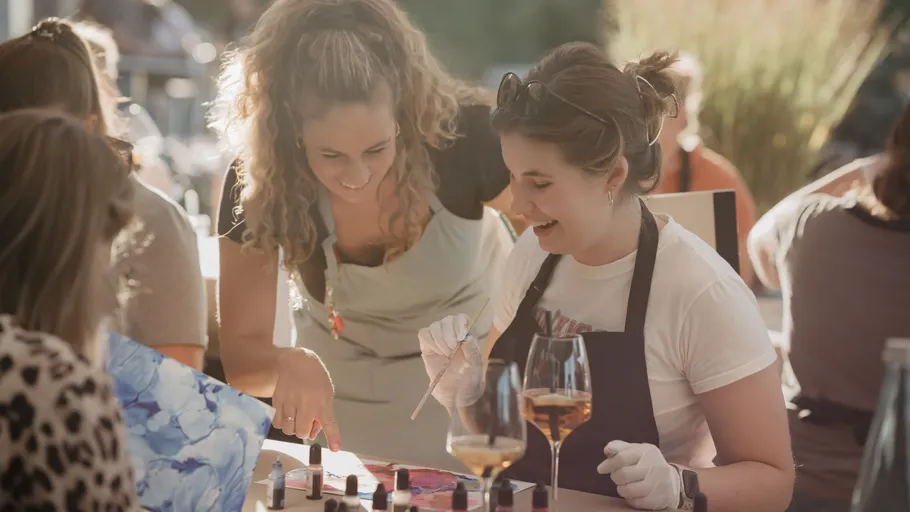 Women painting and smiling outdoors.