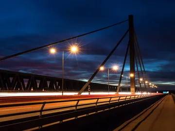 Bridge at night, cars drive across illuminated roadway.