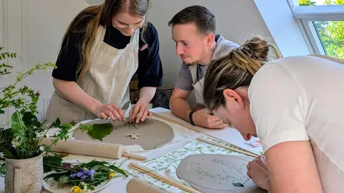 Three people crafting with leaves and flowers indoors.