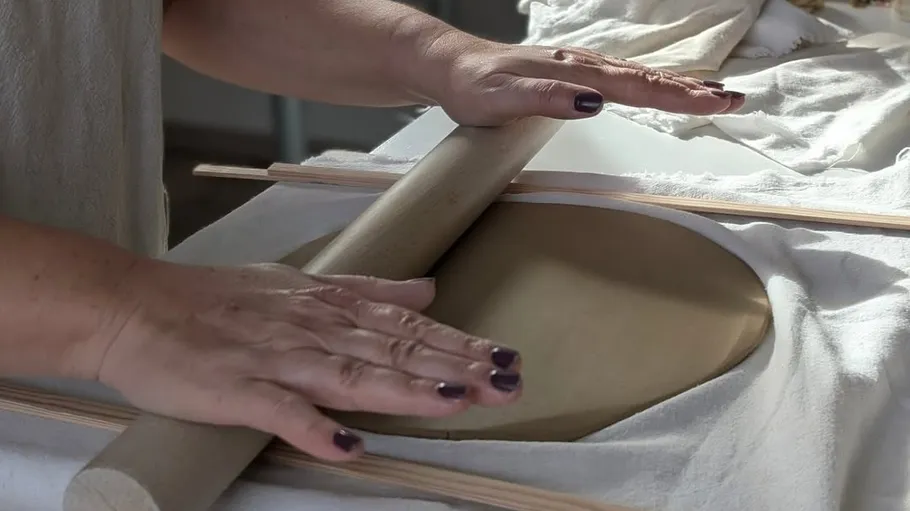 Hände rollen Teig auf einem Tisch.