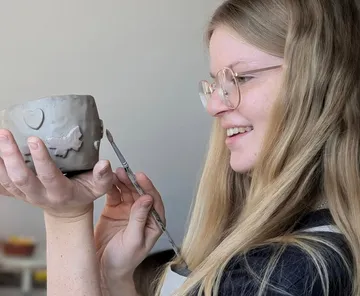 Frau modelliert Tontopf lächelnd drinnen.