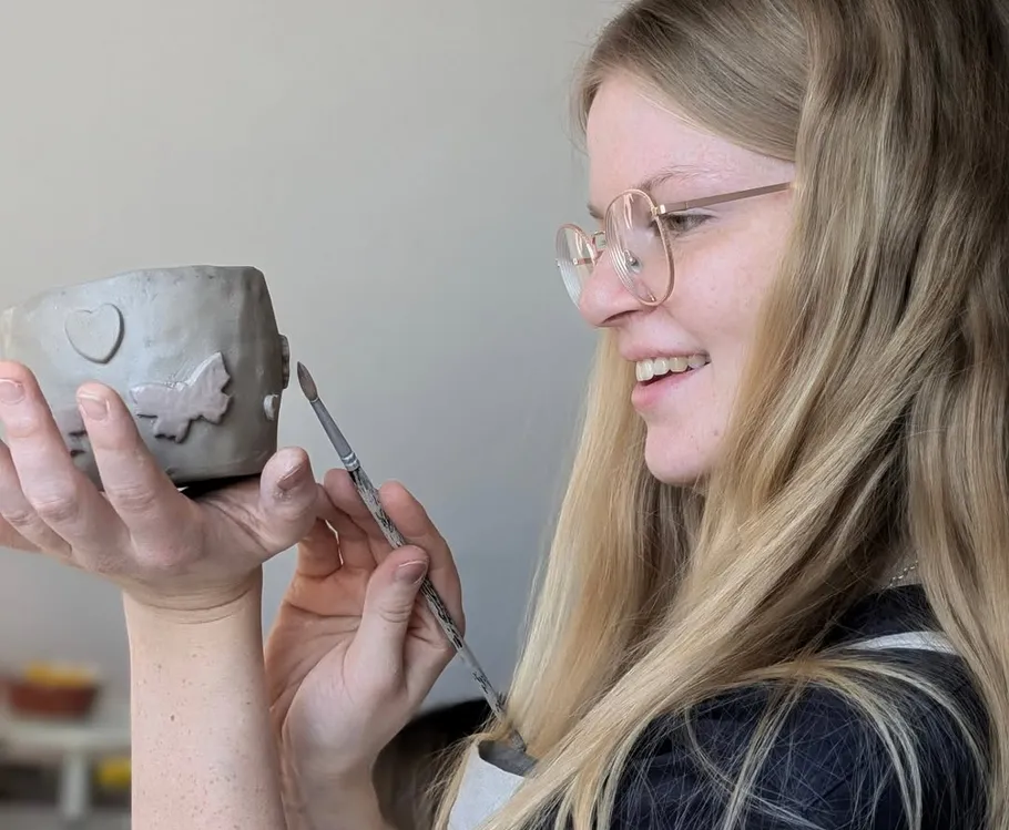 Woman sculpting clay pot with smile indoors.