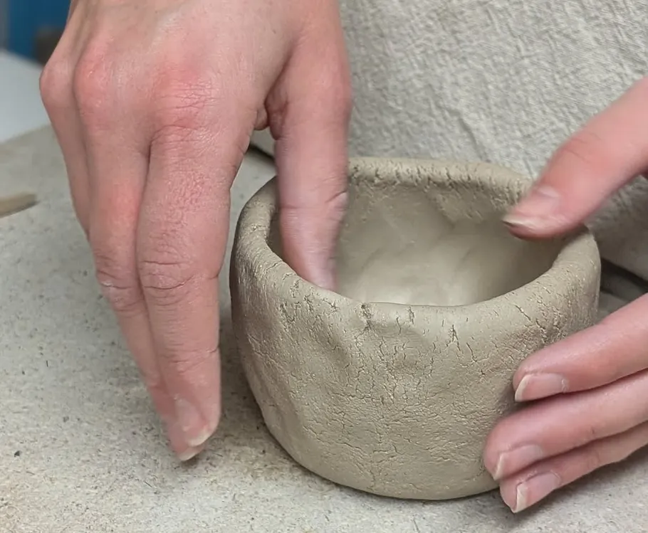 Hands shaping a clay pot on a table.