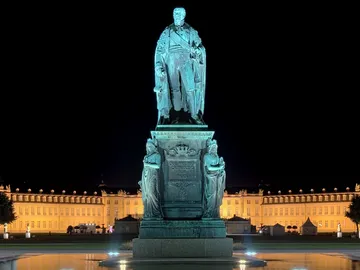 Statue steht beleuchtet, umgeben von einem eleganten Gebäude.