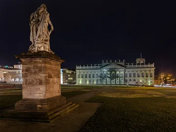 Statue stands, illuminated, in front of a historic building at night.