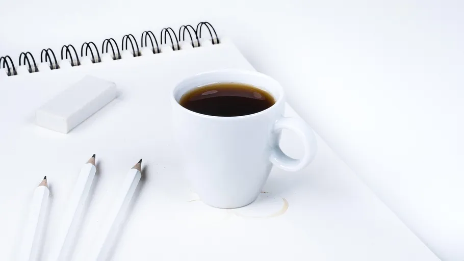 Kaffeetasse auf Notizbuch mit Bleistiften und Radiergummi.