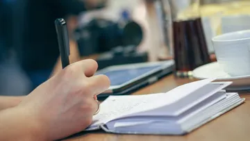 Person writing in notebook at a table.