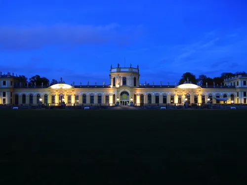 Historic building glows at night, surrounded by green spaces.