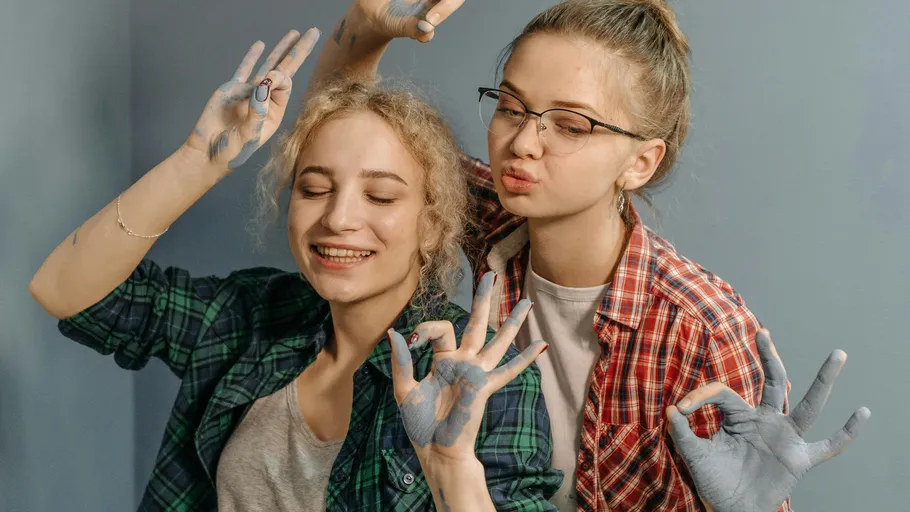 Two women smiling, making hand gestures, indoors.