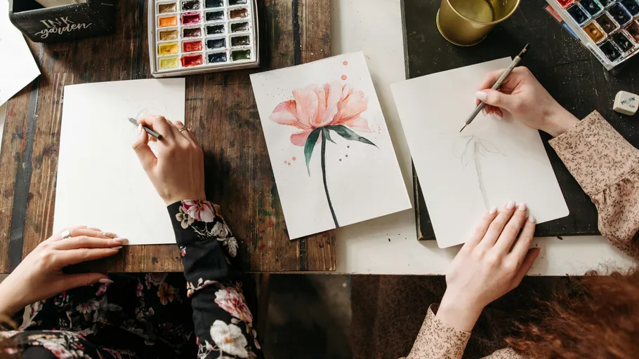 Two people sketching flowers at wooden table.