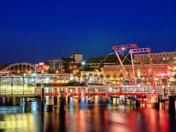 Hafen mit beleuchtetem Steg und städtischer Landschaft bei Nacht.