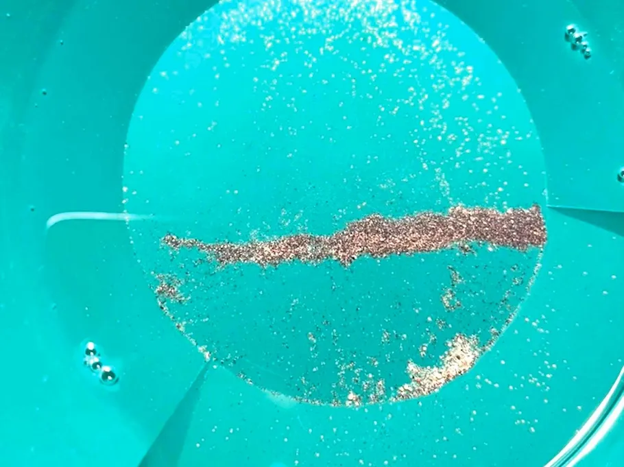 Gold flakes in green pan with water.