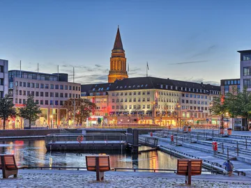 Stadtansicht mit Hafen, Abendstimmung, beleuchtete Gebäude.