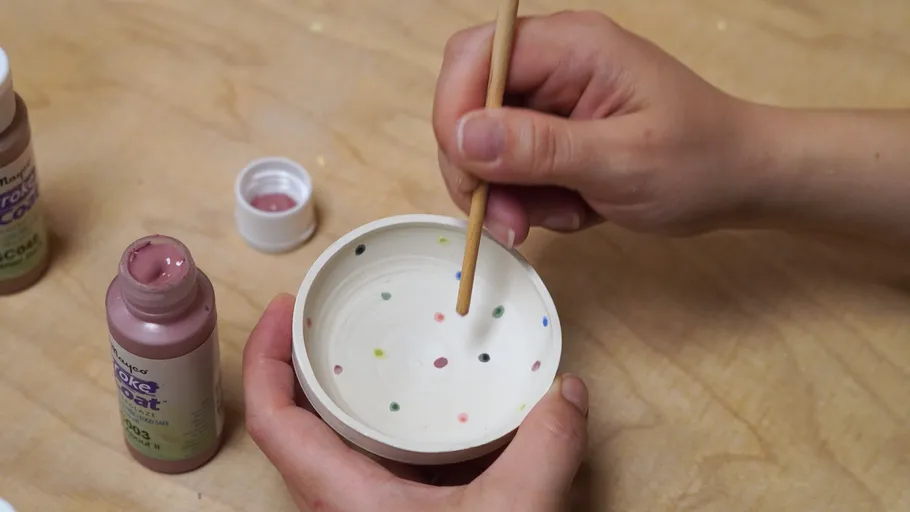 Hands painting dots in ceramic bowl.