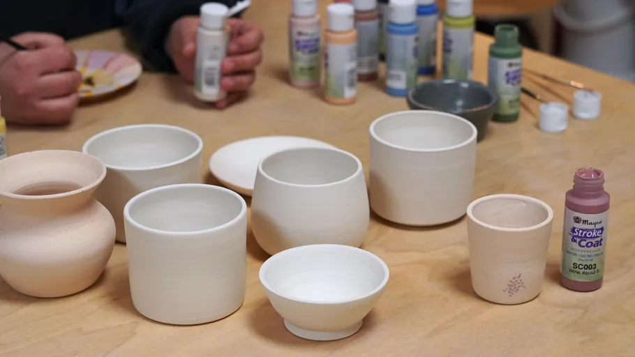 Unfinished pottery cups on table with paints.