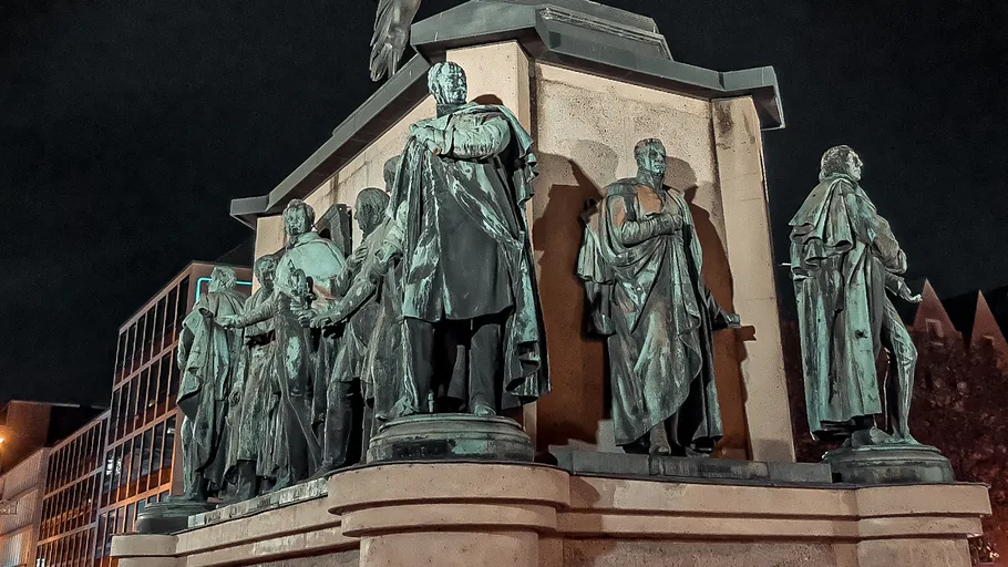 Statues of historical figures at night outdoors.