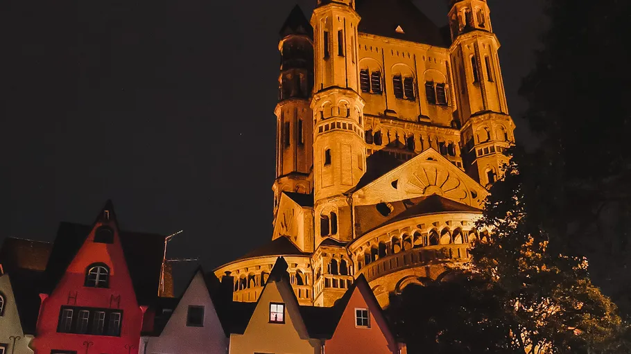 Illuminated cathedral behind colorful houses at night.