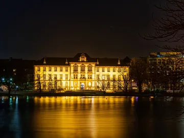 Historisches Gebäude leuchtet am Ufer eines ruhigen Gewässers.