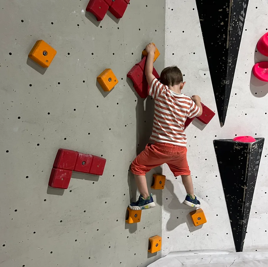 Kind klettert bunter Indoor-Boulderwand.