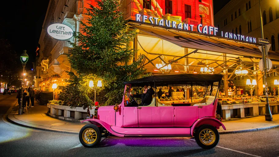 Pink vintage car driving past decorated café.