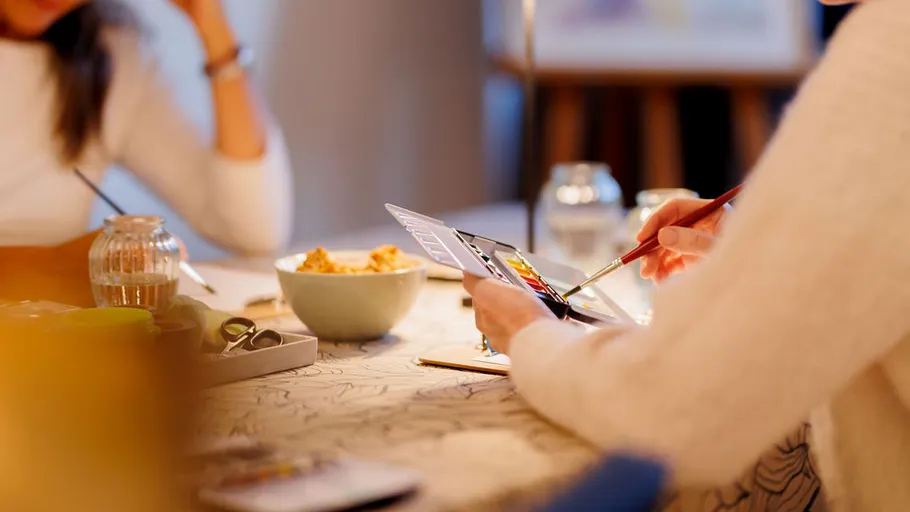 Person painting on tablet, seated at table.