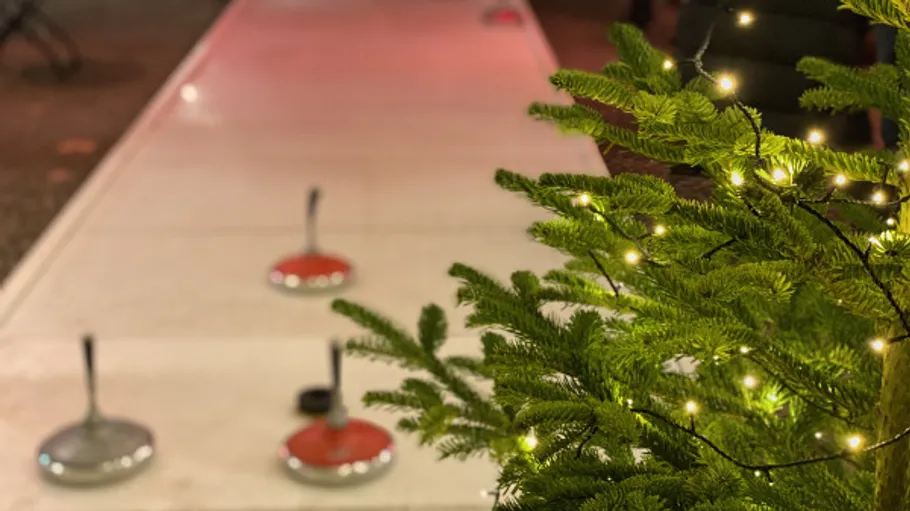 Curling stones on ice near decorated tree.