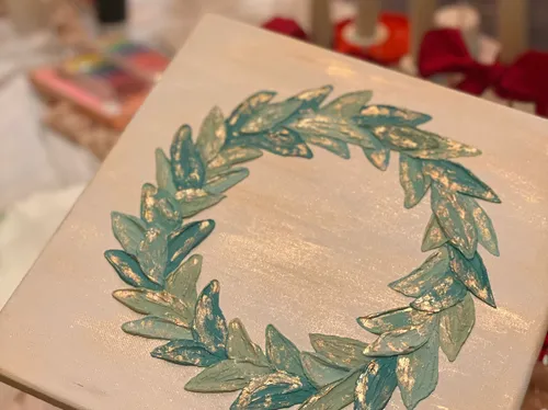 Painted green wreath on canvas, blurred background.