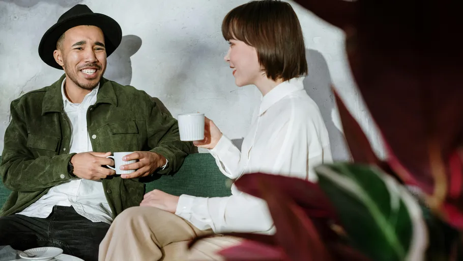 Two people smiling, holding coffee mugs indoors.