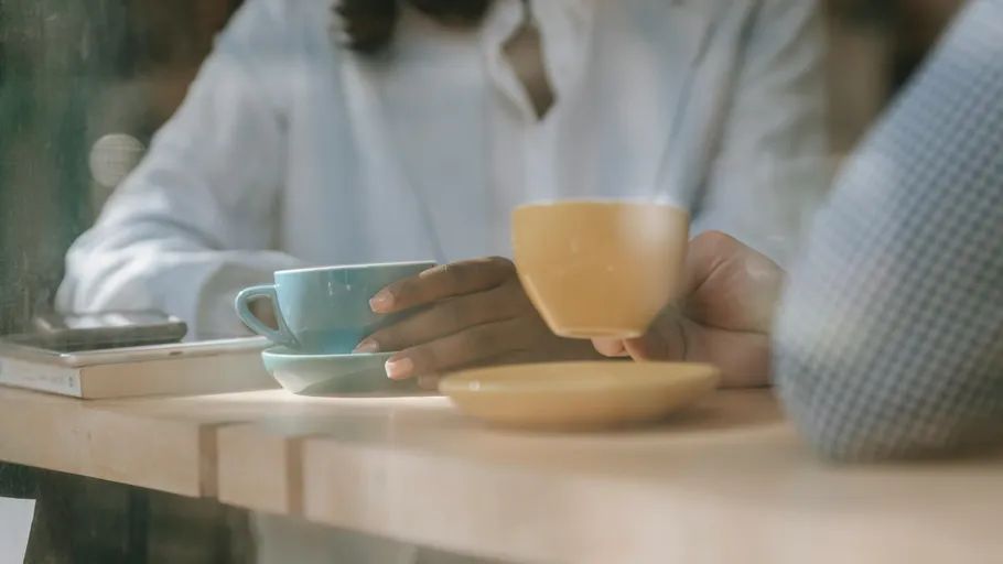 Two hands holding coffee cups at table.