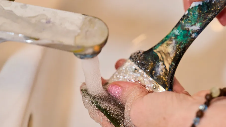 Paintbrush being washed under running faucet.