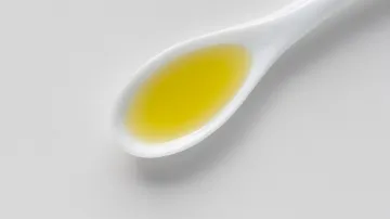 White spoon holds yellow liquid on gray surface.