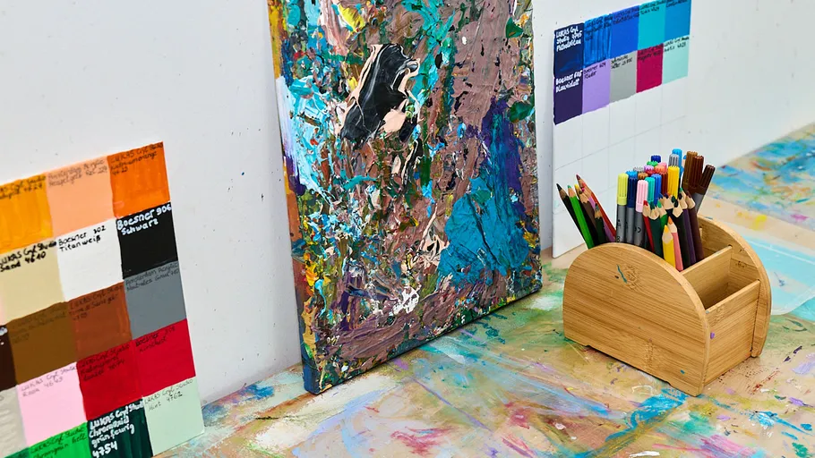 Abstract painting and pencils on messy table.