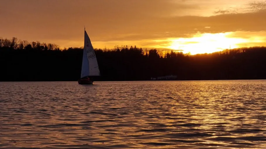 Sailboat on lake during sunset, trees in background.
