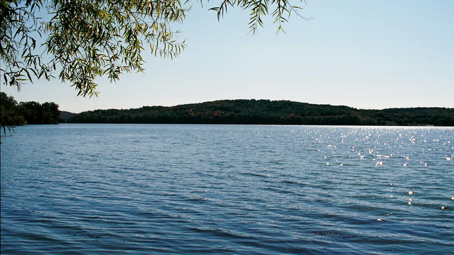 See mit Bäumen und Hügeln im Hintergrund.