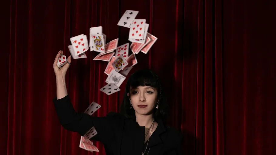 Woman tossing playing cards against red curtain.