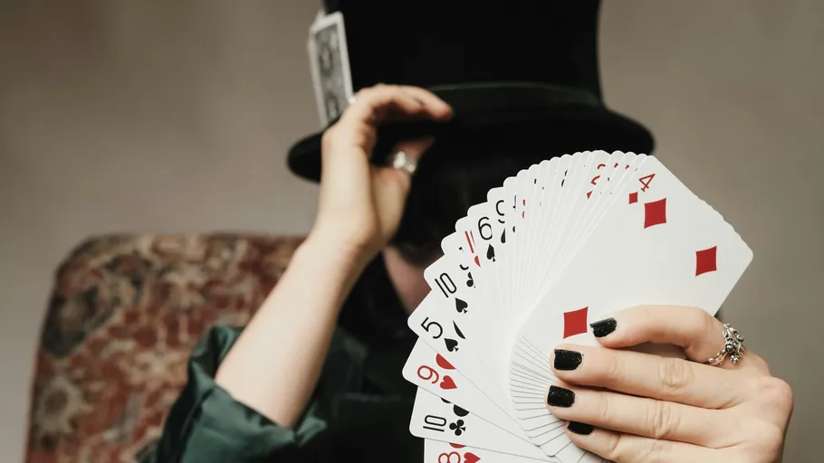 Person holding fanned playing cards, wearing top hat.