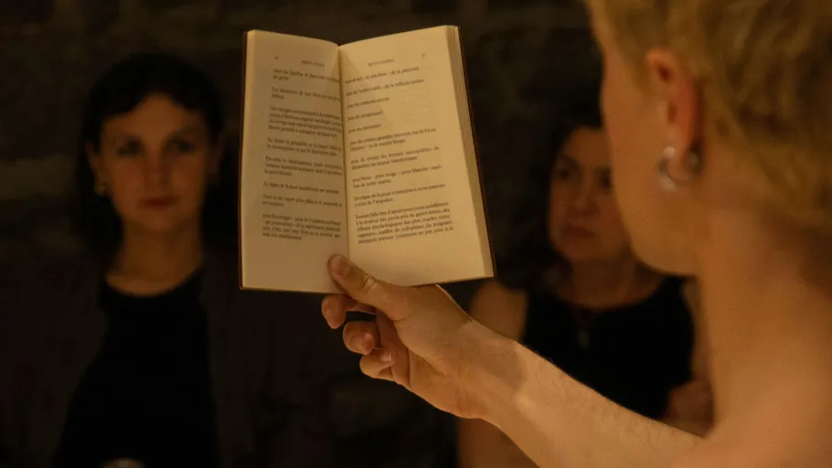Person holds open book, two women listening.