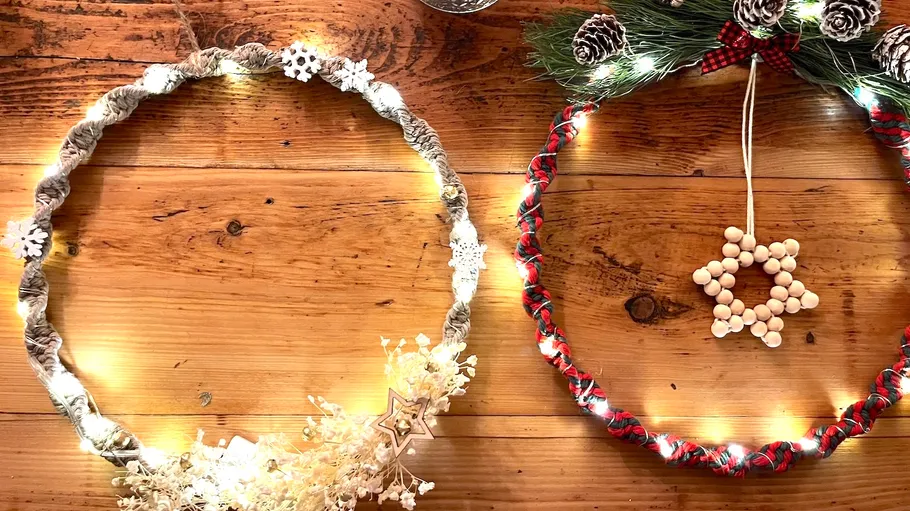 Two decorated wreaths with lights on wooden table.